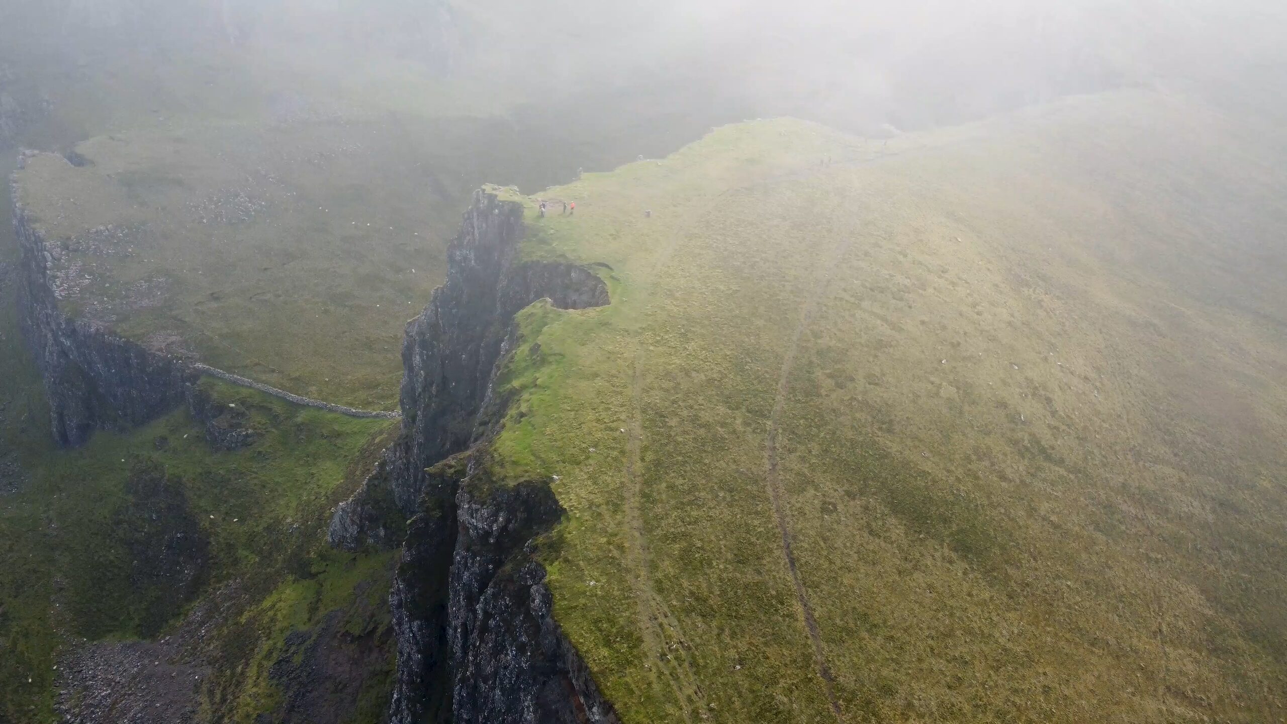 Aerial view of a rocky cliff edge on a green mountain ridge in fog