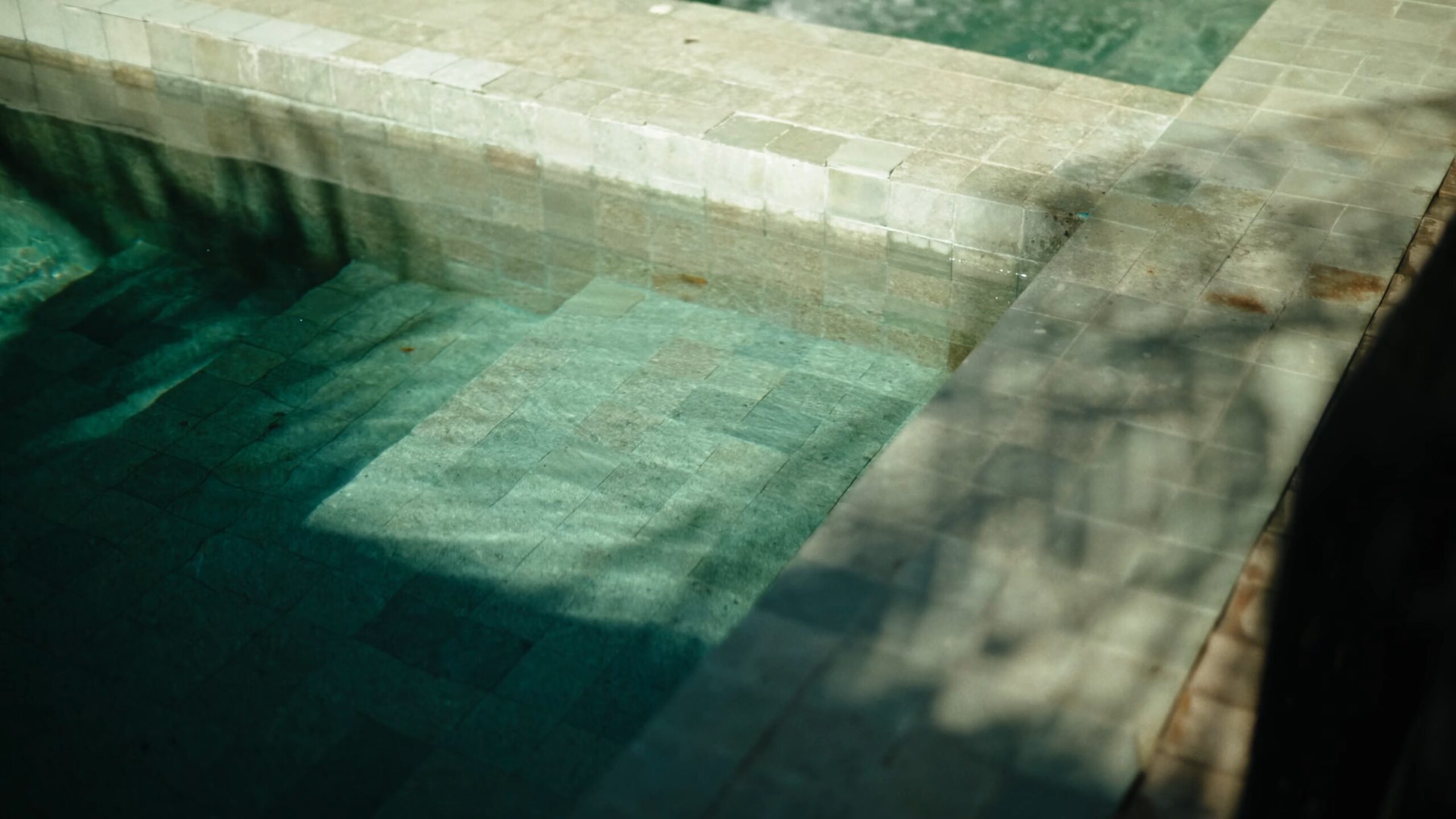 Green stone tiles of a heated pool in soft light and leaf shadows