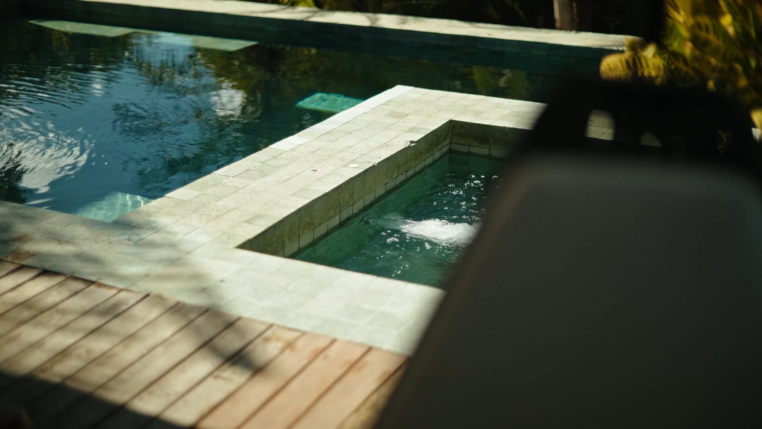 A hot tub set into the tiled edge of a pool, next to a wooden deck